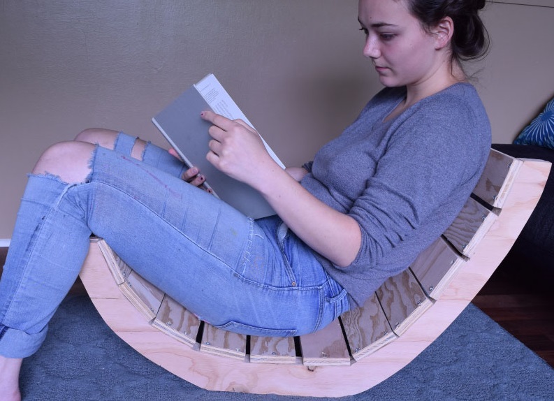 a photo of a u-shaped chain with no legs, sitting on the ground. violet is sitting in it, reading a book. her hair is up, and she's wearing a sweater and ripped jeans